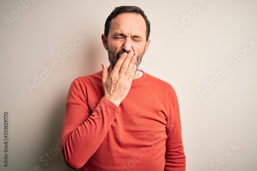Middle age hoary man wearing casual orange sweater standing over isolated white background bored yawning tired covering mouth with hand. Restless and sleepiness.