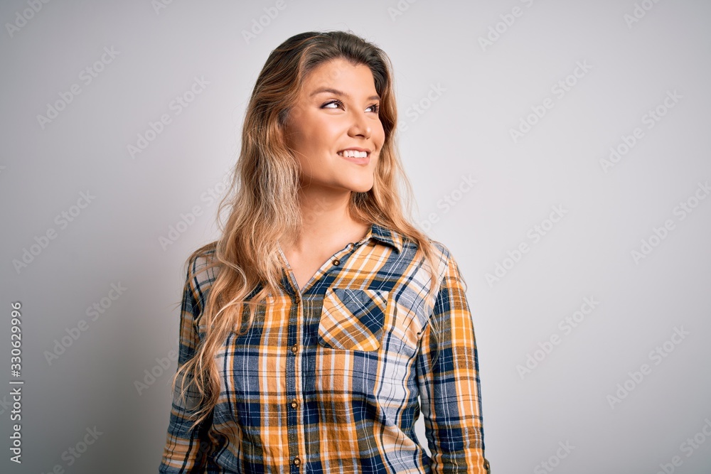 Young beautiful blonde woman wearing casual shirt standing over isolated white background looking away to side with smile on face, natural expression. Laughing confident. Young beautiful blonde woman wearing casual shirt standing over isolated white background looking away to side with smile on face, natural expression. Laughing confident.