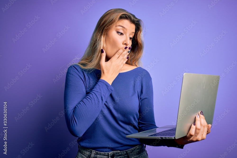 Young beautiful blonde woman working using laptop over isolated purple background cover mouth with hand shocked with shame for mistake, expression of fear, scared in silence, secret concept