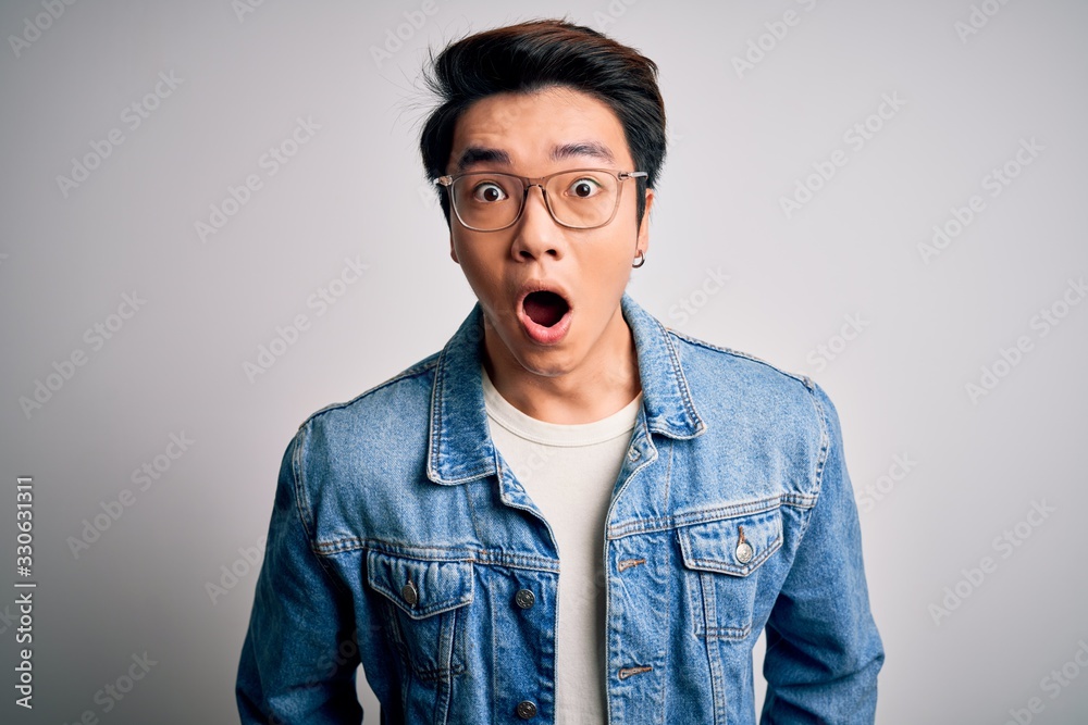 Fototapeta premium Young handsome chinese man wearing denim jacket and glasses over white background afraid and shocked with surprise expression, fear and excited face.