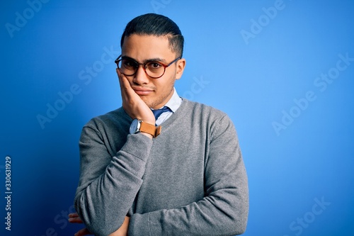 Young brazilian businessman wearing tie standing over isolated blue background thinking looking tired and bored with depression problems with crossed arms.