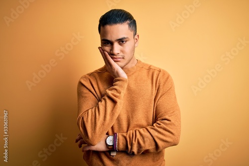 Young brazilian man wearing casual sweater standing over isolated yellow background thinking looking tired and bored with depression problems with crossed arms. © Krakenimages.com