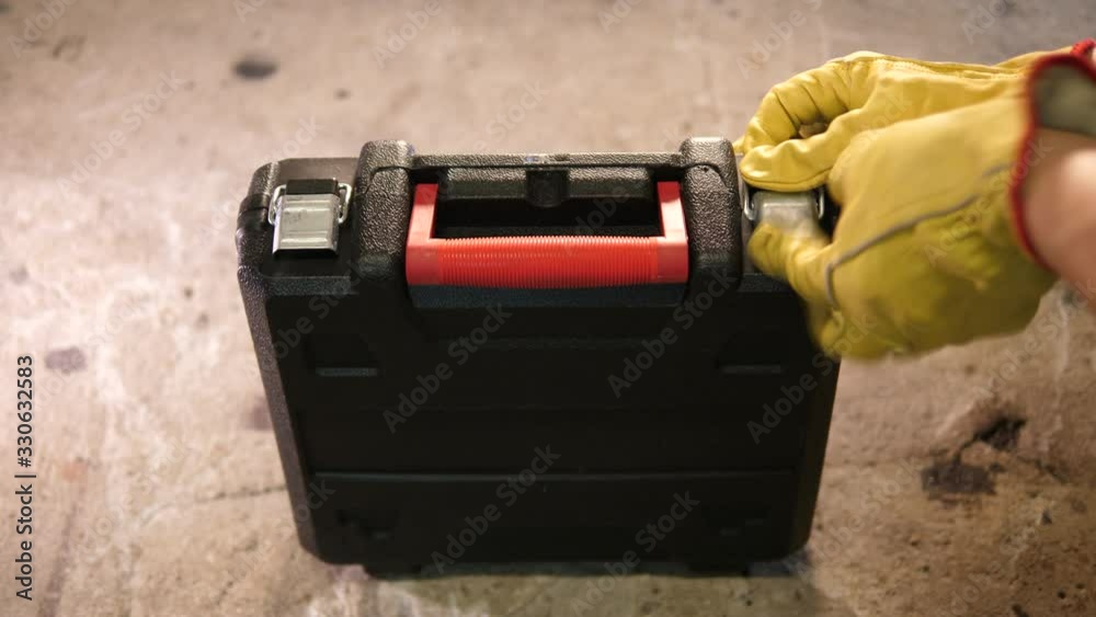 Construction worker closing locking plastic new Tooldbox in the garage. Worker with yellow gloves. Construction worker closing locking plastic new Tooldbox in the garage. Worker with yellow gloves.