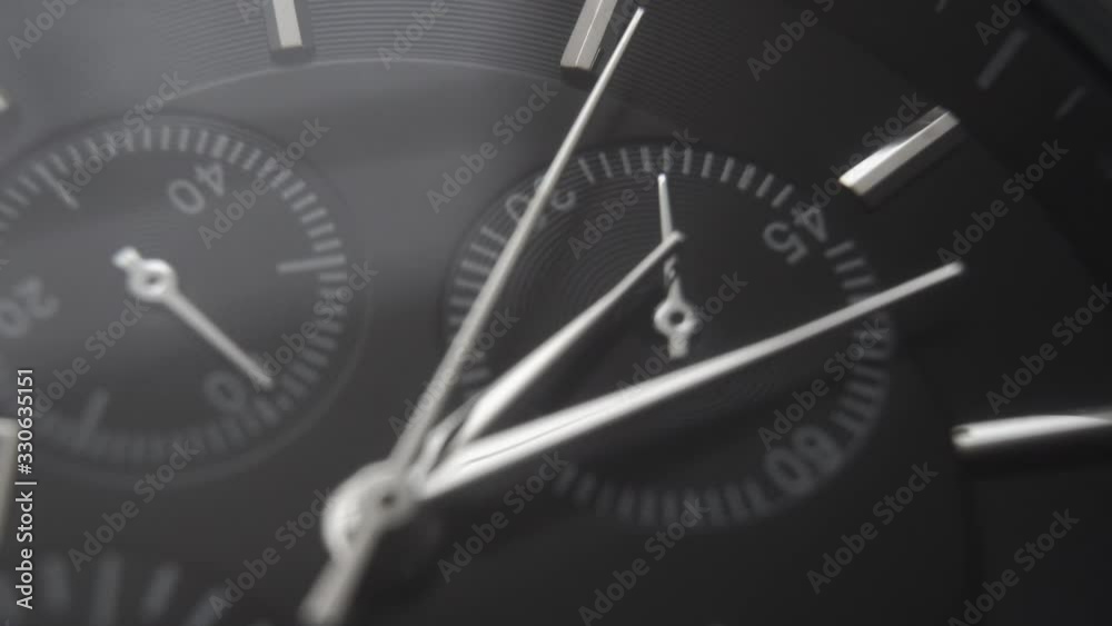 Metallic dark wristwatch with silver hands on a black background. Macro shot.