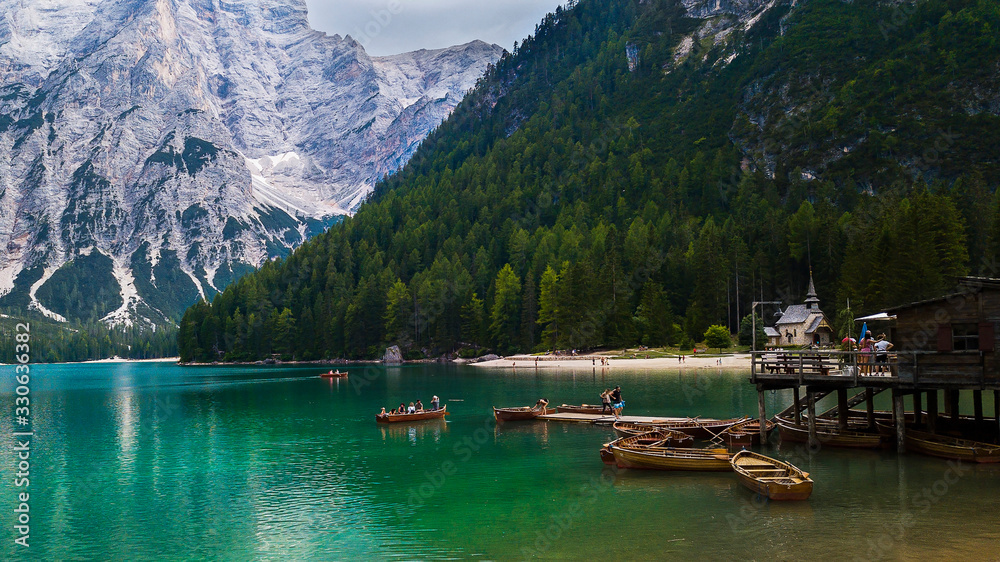 View Braies Lake, Dolmites mountain, water reflections, pier with boats