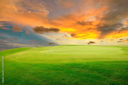 Green grass field and colorful sky clouds at sunset.