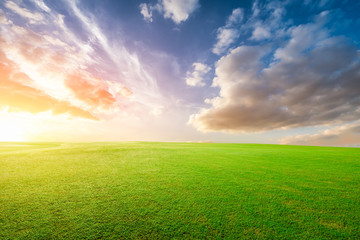 Green grass field and colorful sky clouds at sunset.