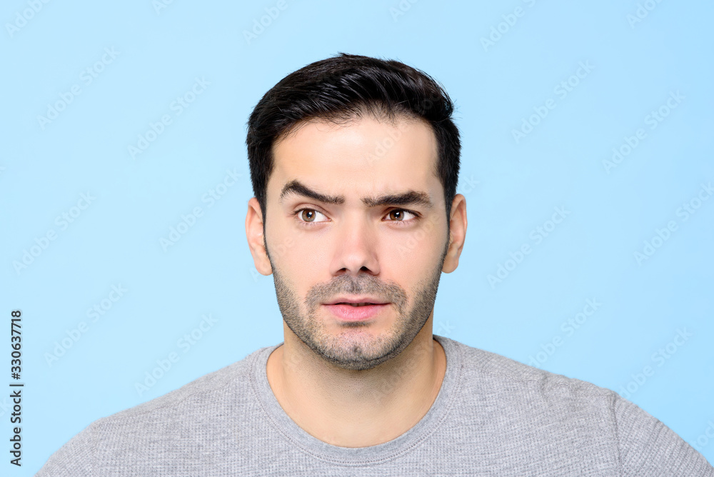 Fototapeta premium Thoughtful curious young man face with eyebrow raised isolated on light blue backgound
