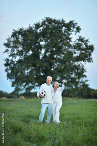 Happy beautiful senior couple in summer field with ball