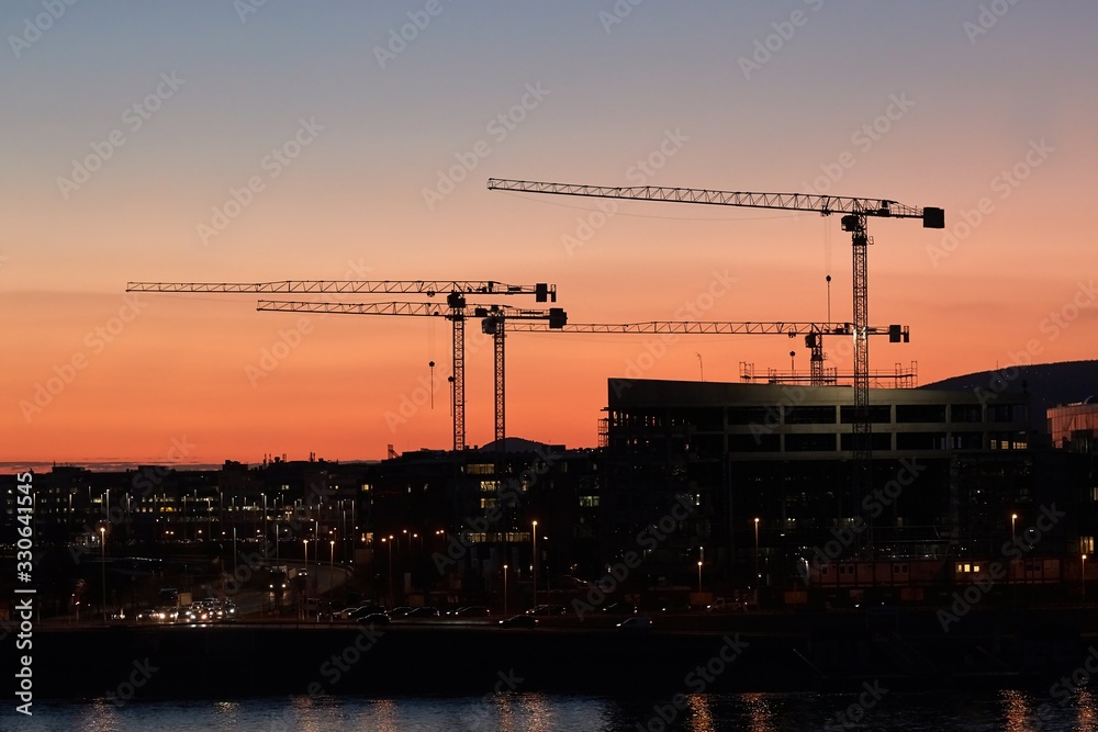 Construction cranes against dramatic twilight red glow sky