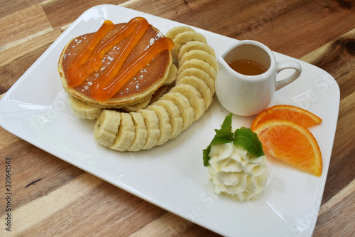 Pancakes with banana, orange sauce and caramel on wooden background