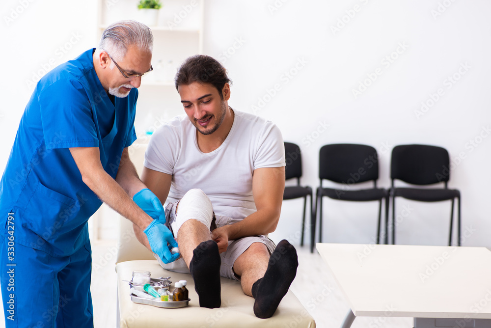 Leg injured man visiting old doctor in first aid concept Leg injured man visiting old doctor in first aid concept