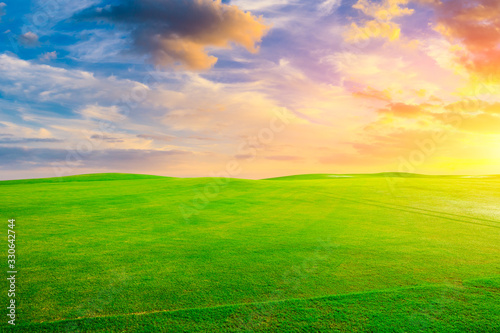 Green grass field and colorful sky clouds at sunset.