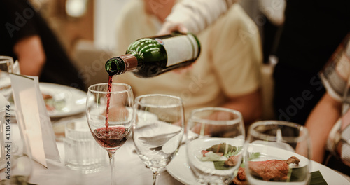Waitress is pouring red wine in glasses for wine tasting event on the table in restaurant . Blurred background. wine, tasting, pour, bartender, beverage, dinner concept.