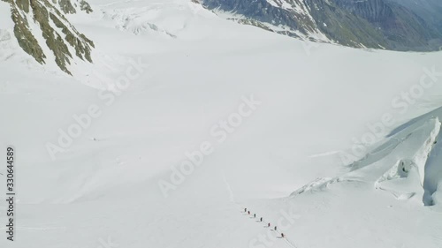 Aerial fly above tourists climbs up on spacious snow slope, mountain expedition