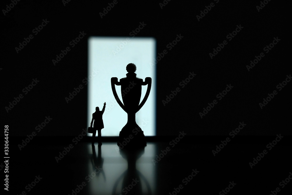 Obraz premium Business strategy conceptual photo - Silhouette of miniature businessman pointing on winning trophy in the podium