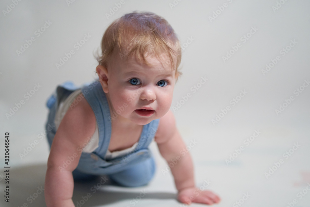 emotional portrait of a one-year-old baby in denim overalls on a uniform light background emotional portrait of a one-year-old baby in denim overalls on a uniform light background