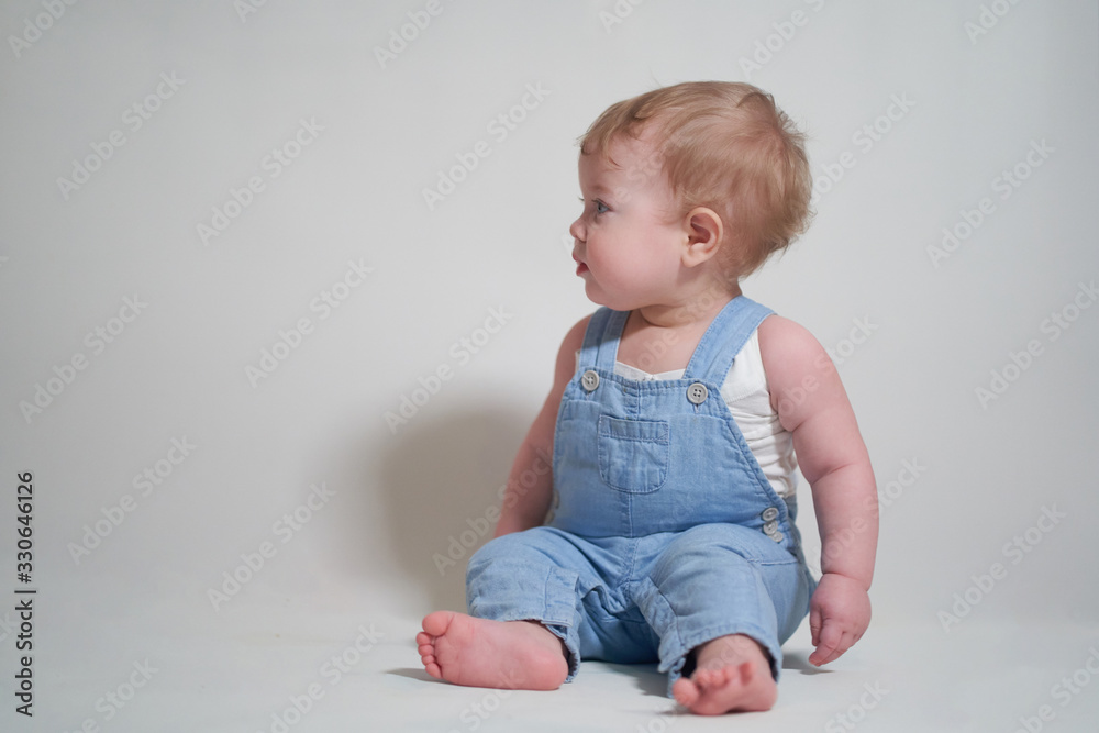 emotional portrait of a one-year-old baby in denim overalls on a uniform light background emotional portrait of a one-year-old baby in denim overalls on a uniform light background