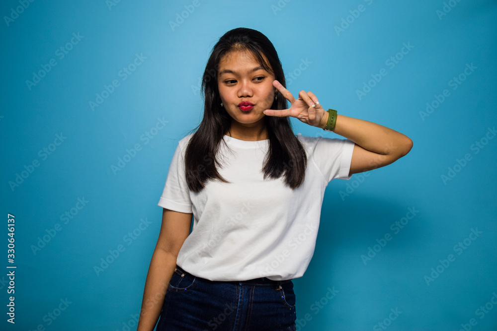 Portrait of Young beautiful asian women using white T-shirt with blue isolated background, showing peace sign and smiling, Victory sign, two sign Portrait of Young beautiful asian women using white T-shirt with blue isolated background, showing peace sign and smiling, Victory sign, two sign