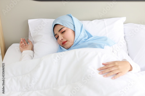 Oversleeping asian muslim woman wearing white sleepwear lying on bed with happiness.Top view portrait young cute girl sleeping in bedroom with happy and beauty face. Lifestyle concept photo