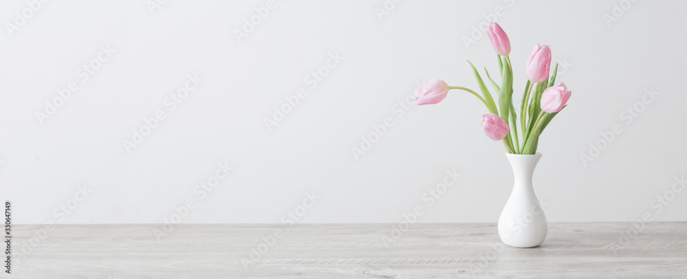 pink tulips in white ceramic vase on wooden table on background white wall - obrazy, fototapety, plakaty 