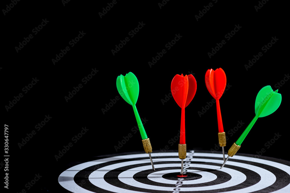 Red and green dart arrow hitting target center is Dart board Isolated on black background Red and green dart arrow hitting target center is Dart board Isolated on black background
