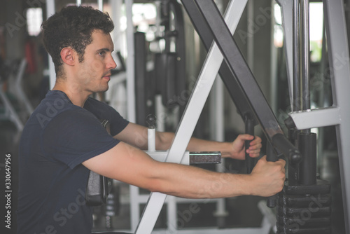 Handsome man lowering weight of fitness machine and working out in the fitness gym