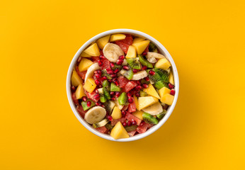 Mixed fruit salad in plate on yellow background top view Diet summer food concept