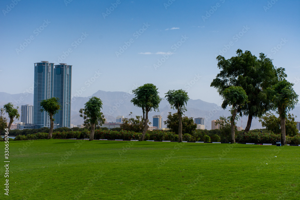 Ras al Khaimah, United Arab Emirates Corniche with green grass picnic and family area, looking towards the mountains on a sunny day.