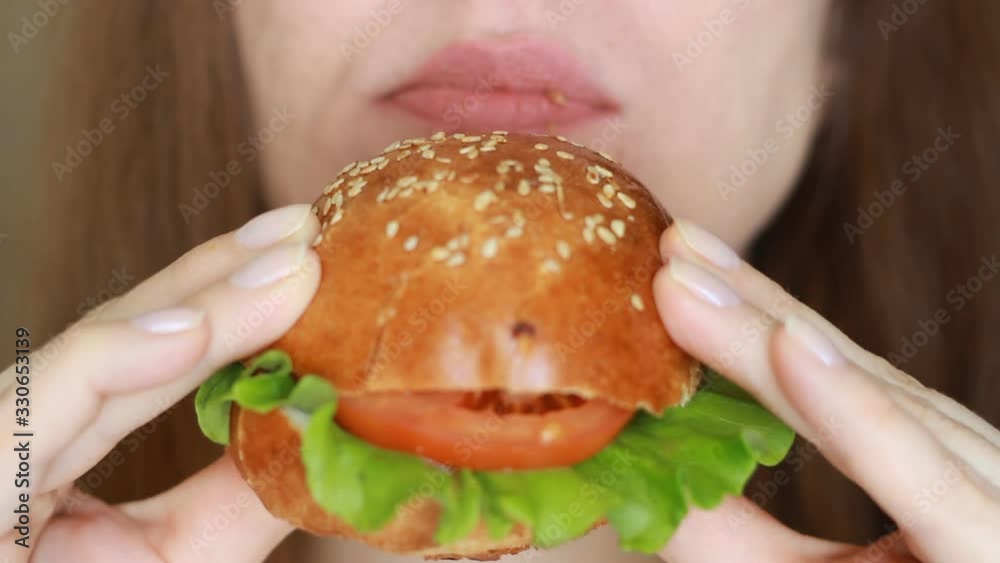 Woman biting a burger closeup. Woman eating a hamburger. Woman biting a burger closeup. Woman eating a hamburger.