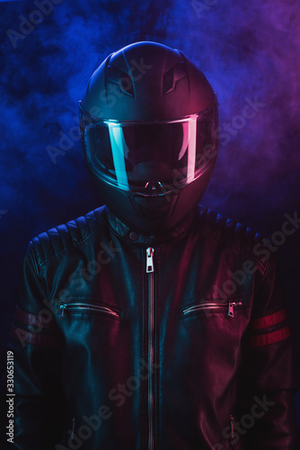 A guy in a motorcycle helmet and leather jacket against a background of neon lights and smoke