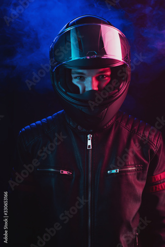 A guy in a motorcycle helmet and leather jacket against a background of neon lights and smoke © Антон Фрунзе