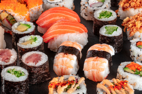 Large sushi set, close-up on a black background. An assortment of various maki, nigiri and rolls