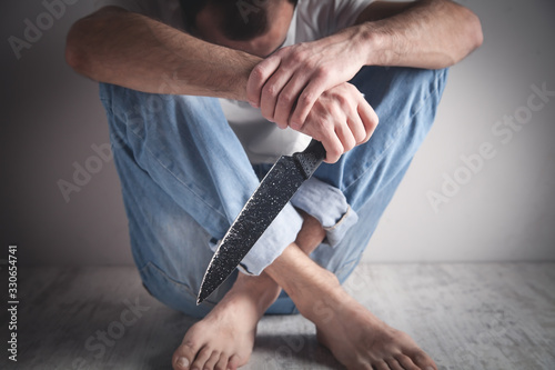 Sad man sitting in room with a knife.