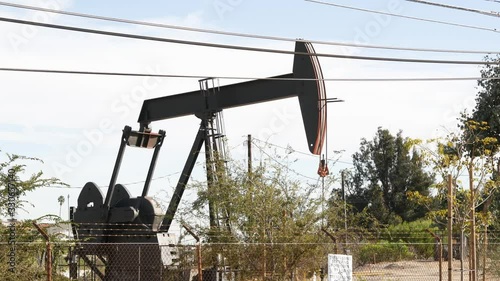 Industrial urban landscape. La Brea Inglewood in Los Angeles. Well pump jack operating behind the fence. Drilling rig extract crude oil. Oil mining machine with working piston. Oil and gas industry.
