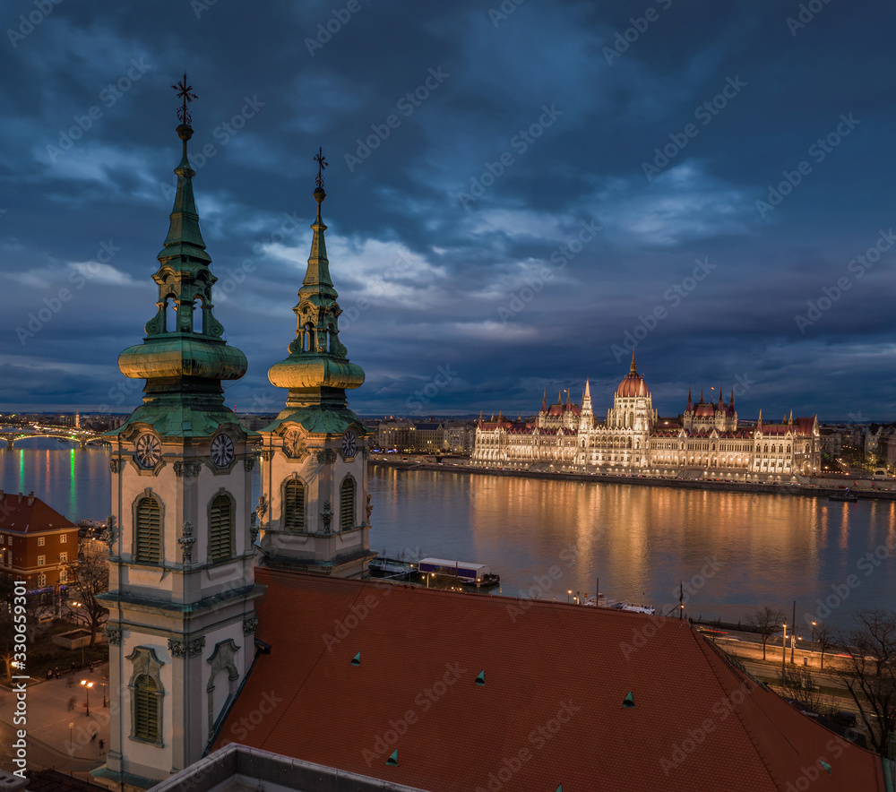 Fototapeta premium Budapeszt, Węgry - widok z lotu ptaka kościoła parafialnego św.Anny na placu Batthyany o zmierzchu z oświetlonym budynkiem parlamentu węgierskiego w tle