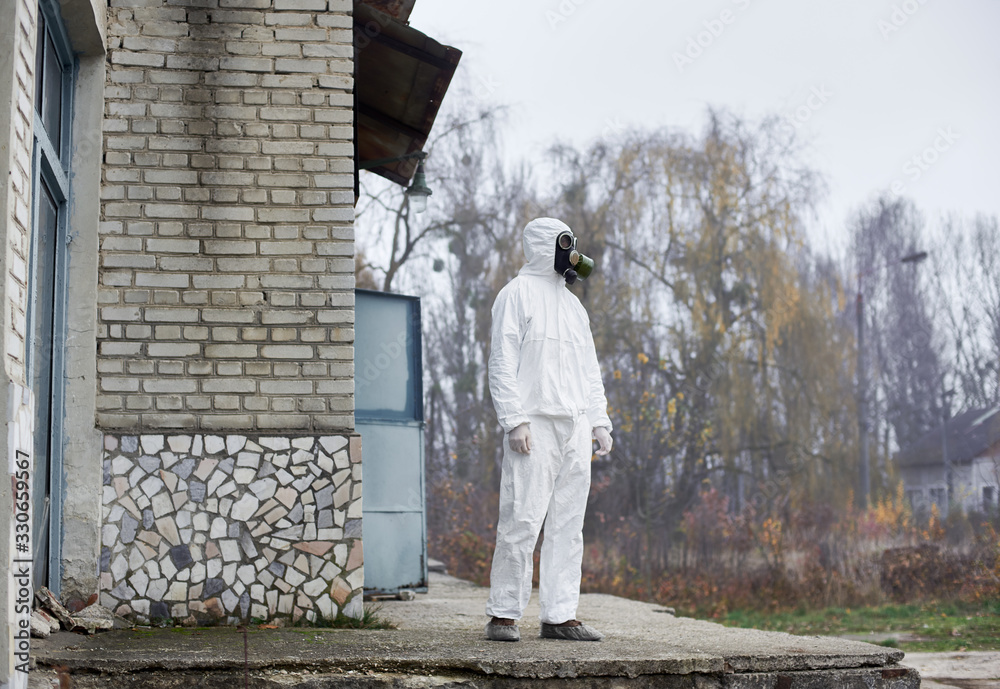 Male research scientist standing outside while working at thermal power station. Environmentalist wearing white protective suit and gas mask. Concept of ecology and environmental pollution.
