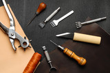 Leather crafting DIY tools lies on natural black and brown leather.