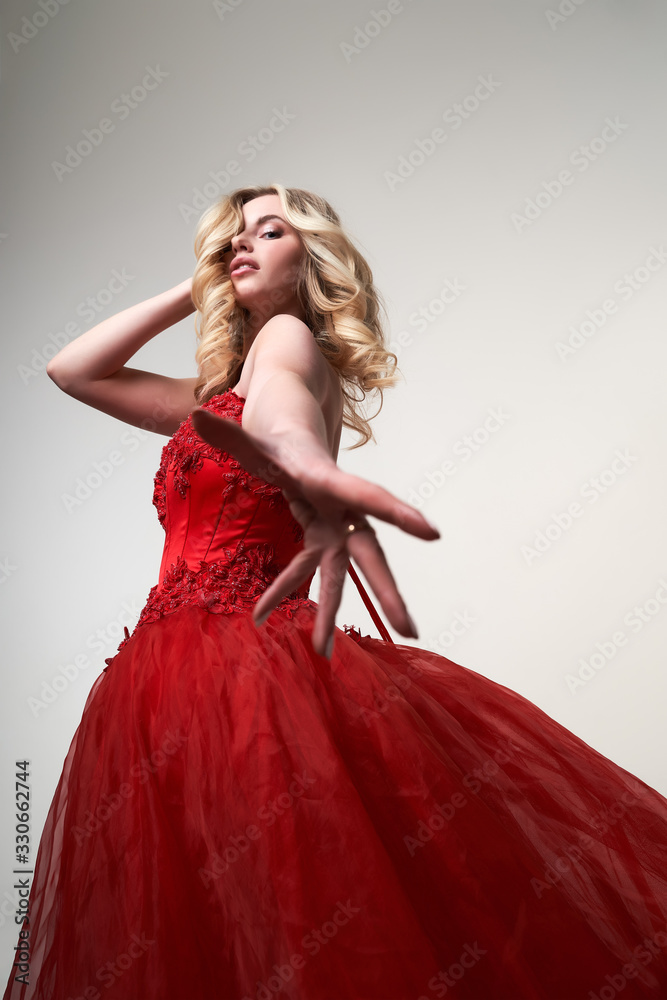 Young blonde woman in long red dress with outstretched hand in studio