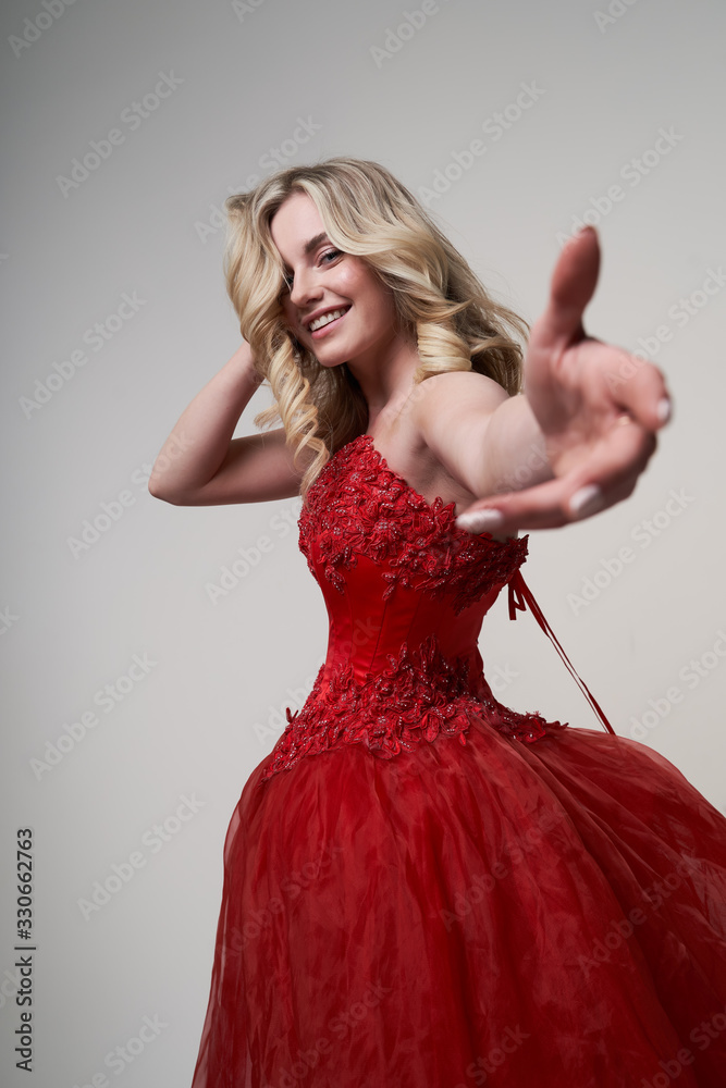 Happy blonde in long red dress with outstretched hand in studio