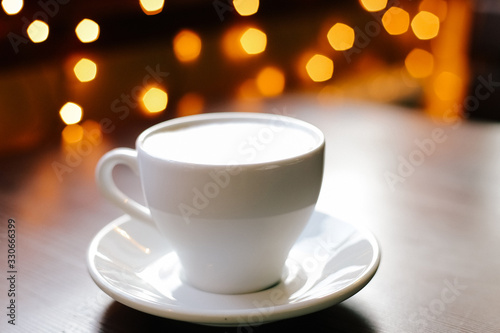 A cup of coffee on wooden table. Lights on the background. Front view.