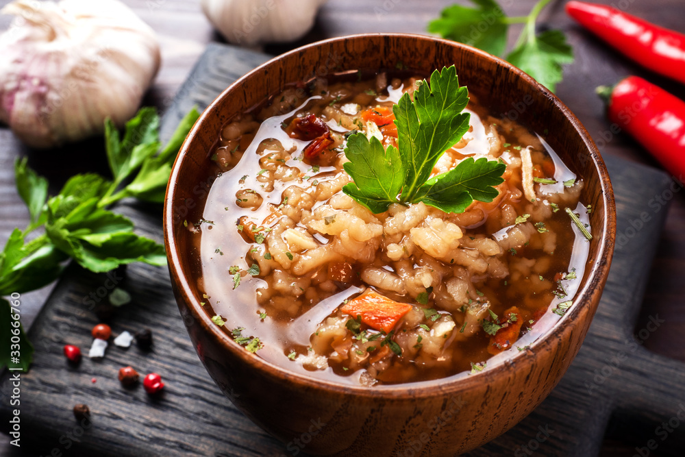 Vegetarian soup kharcho with rice and vegetables. Garlic hot pepper tomatoes. Wooden rustic background, plates made of natural bamboo. Vegetarian soup kharcho with rice and vegetables. Garlic hot pepper tomatoes. Wooden rustic background, plates made of natural bamboo.