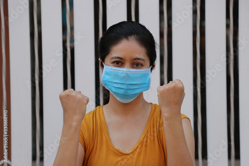 Masked Asian woman prevent germs. Tiny Particle or virus corona or Covid 19 protection. Lift the fist up for meaning fighting illness.