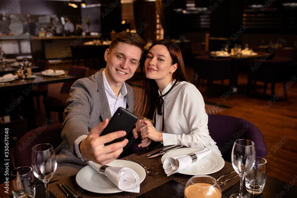 man and woman take selfie in luxury restaurant. they have dinner together, take photo of themselves, smile and celebrate anniversary, dating. indoors