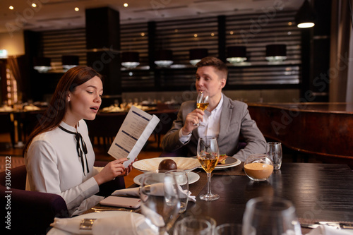 caucasian couple in restaurant. young girl reads the menu  wants to make an order. handsome guy sit looking at her and waiting for her order