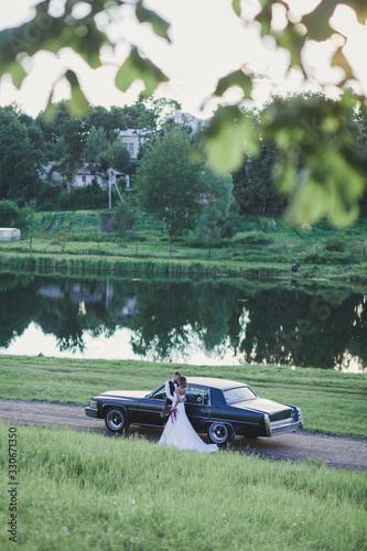 Happy bride and groom hugging near old retro car outdoors