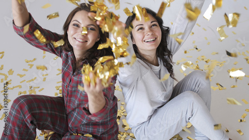 Beautiful happy women throwing gold glitter confetti on a white background