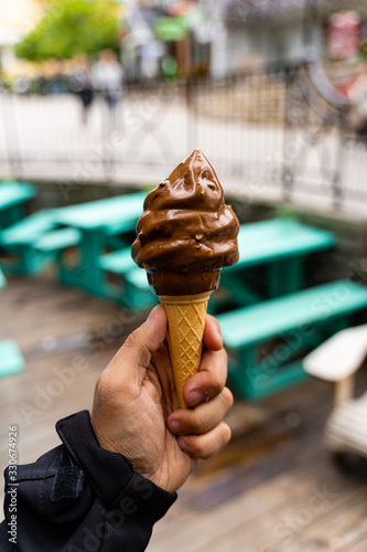 фотографія Man holding dipped chocolate ice cream cone in hand, very blurred background, small depth of field