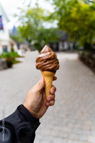 Man holding dipped chocolate ice cream cone in hand, very blurred background, small depth of field. Dark background. photo