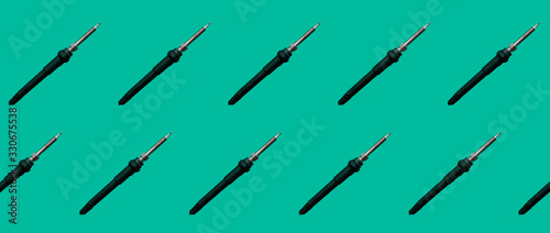 Template of inclined soldering irons. Soldering irons have black coils and a metal tip. Ten soldering irons are depicted on a plain green background. Template for wrapping paper.
